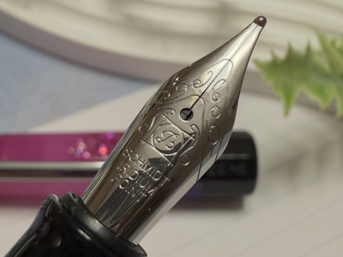 Close-up of a fountain pen nib and upper barrel, showing engraved decorative details on the metal nib.